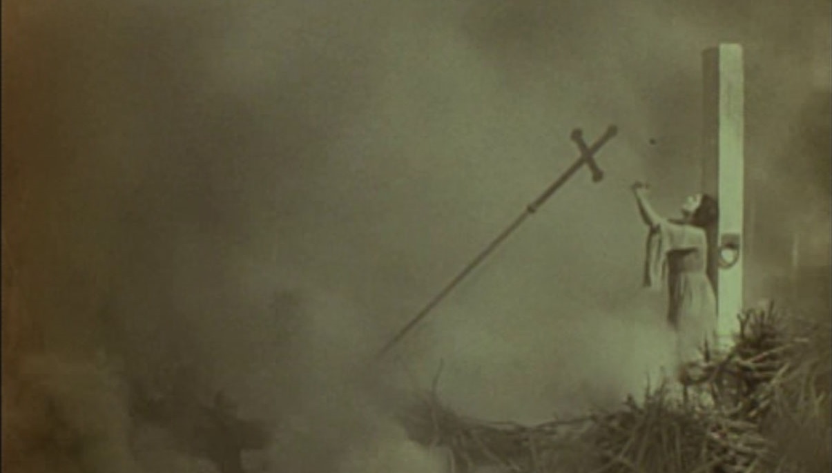A priest holds up a cross in Joan the Woman (1916).